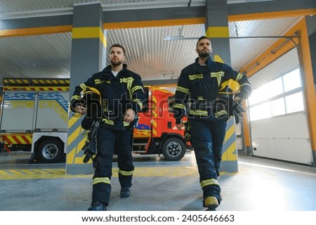 Two firefighters in protective clothing in helmets with fire engine.