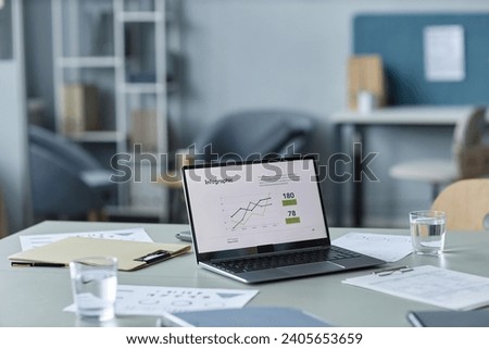 Medium shot of desk with operating laptop with chart on screen, water glasses and clipboards with papers prepared for business meeting in modern office