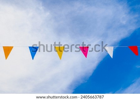 Colourful flag waving in the air on sky, Multicolour of pennant flags (Orange, Blue, Yellow, Red and White) hanging on the rope with clear sky and clouds background, Free copy space for your text.