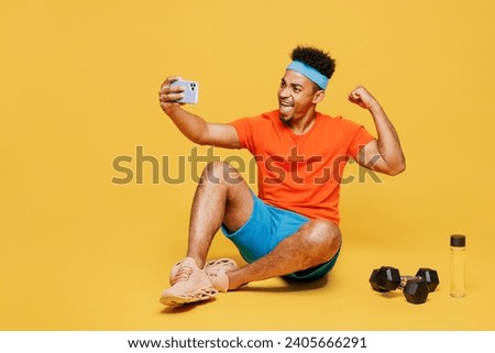 Full body young fitness trainer sporty man sportsman wear orange t-shirt do selfie shot on mobile cell phone spend time in home gym isolated on plain yellow background. Workout sport fit abs concept