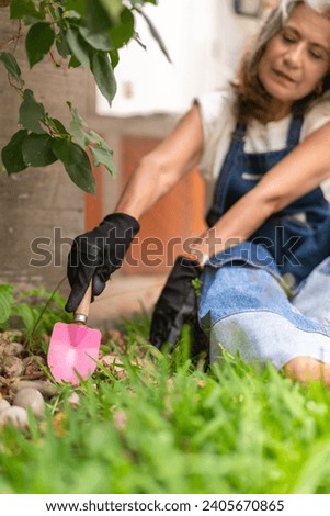 Vertical photo of a mature woman planting flowers using a small shovel at home