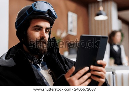 Detailed view of winter traveler holding tablet in hotel lobby, surfing the net for their snowy adventure. Close-up of man grasping a smart device for research on winter holiday activity.