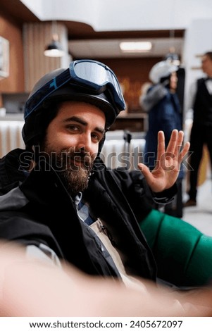 Excited caucasian man at exclusive ski resort holding mobile device for selfie photo. POV of enthuisiastic male tourist dressed in winter jacket, ski goggles and helmet ready for wintersport adventure