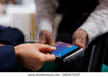 Close-up view of pair of hands grasping credit card and pos terminal at exclusive hotel reception. Detailed shot of person paying for reservation in lounge area of ski mountain resort. Royalty-Free Stock Photo #2405672107