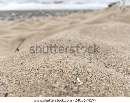 Grains of sand form a tiny part of a huge beach in peak summer. Picture shows a tiny section of a sand dune with the grains of sand in focus. Sea and stones in background. 