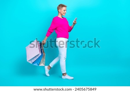 Full size photo of positive woman dressed sweater hold shopping bags look at smartphone go empty space isolated on teal color background