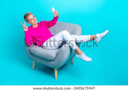 Full size portrait of charming friendly girl sit chair hold smart phone make selfie show v-sign isolated on turquoise color background