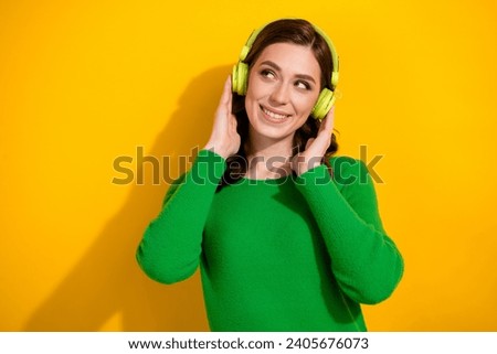 Portrait photo of young charming lady wearing green jumper listen earphones look empty space radio isolated on yellow color background