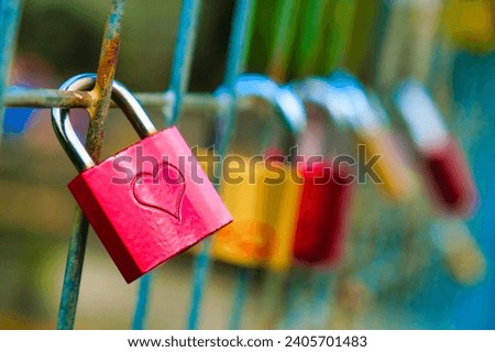 A padlock, a key lock with heart-shaped love signs, is being locked into a bridge rail. Royalty-Free Stock Photo #2405701483