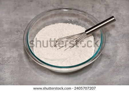 Whole wheat white flour in a glass mixing bowl and a whisk inside.