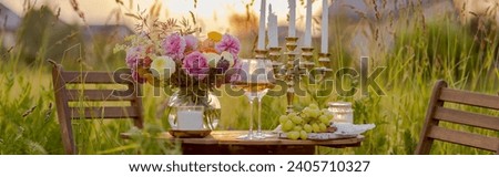 Elegant wedding or private party for a loving couple table setting outdoors in the garden. Beautiful decor with fresh ranunculi flowers, candles. Gourmet cheese board, fruits, white wine. Banner