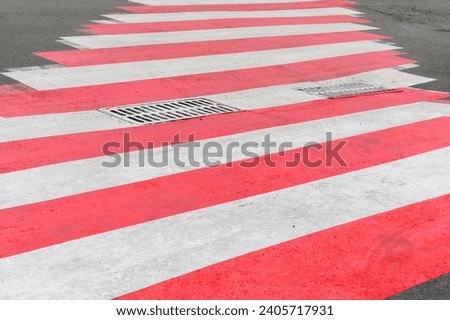 It is a zebra crossing with the red and white rows. It is a close up view of a red zebra