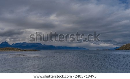 A calm seascape. Islets in the Beagle Channel. Ripples on the ocean surface. Mountains against a background of blue sky and clouds. Argentina. Tierra del Fuego Archipelago