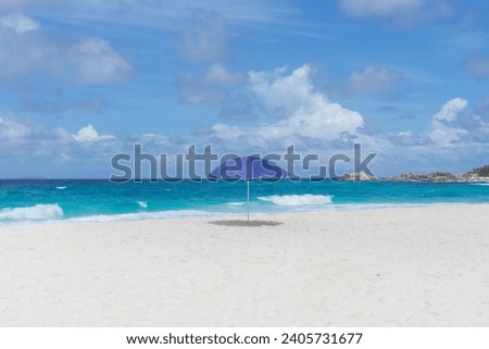 landscape photography of paradise beach with turquoise sea, blue sky and white sand with a blue beach umbrella.