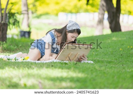 Asian teenage girl drawing a picture in the park with easel, palette, and paintbrush
