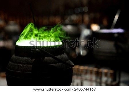 Magic cauldron with mysterious potion and green smoke light from a vintage black pot when wizard cooking and mix dark spell in the fantasy magician for Spooky Halloween Royalty-Free Stock Photo #2405744169