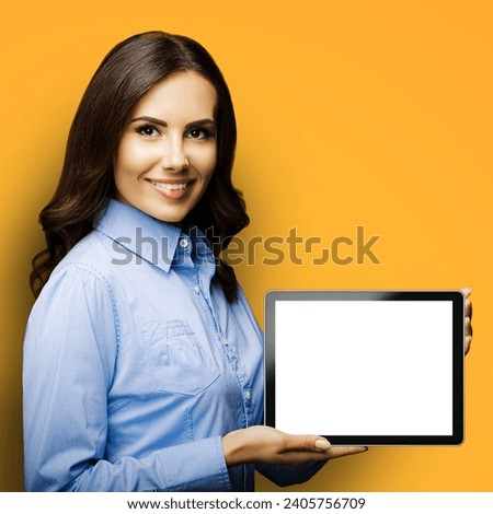 Portrait of cheerfully smiling brunette businesswoman showing mock up blank tablet pc, touchpad, with copy space area for text, yellow background. Confident young business woman. Square photo.