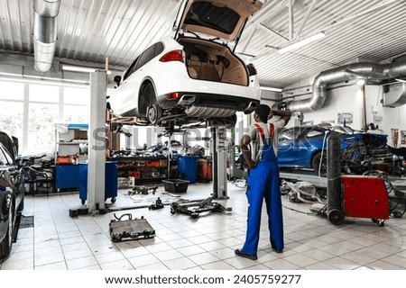 Pensive young African mechanic in car service looking at car thinking of how to repair it Royalty-Free Stock Photo #2405759277