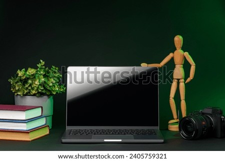 Open laptop with wooden mannequin on table against black background