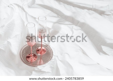 Pink color shining champagne glasses on bed, on white blanket. Lifestyle aesthetic photo, star filter effect. Valentine's Day, love concept, romance meeting. Festive Sparkling wine in wineglasses.