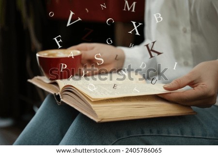 Woman with cup of coffee reading book indoors, closeup. Letters over book