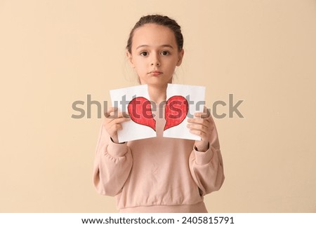 Sad little girl with torn drawing of heart on beige background. Divorce concept