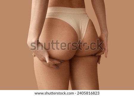 Young woman in panties on beige background, back view. Plastic surgery concept