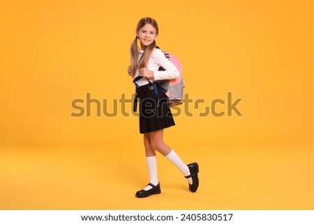 Happy schoolgirl with backpack on orange background Royalty-Free Stock Photo #2405830517