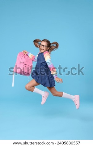 Happy schoolgirl with backpack jumping on light blue background Royalty-Free Stock Photo #2405830557