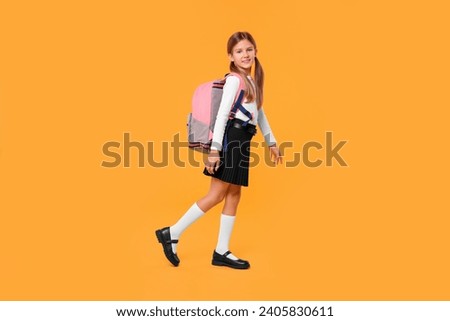 Happy schoolgirl with backpack on orange background Royalty-Free Stock Photo #2405830611