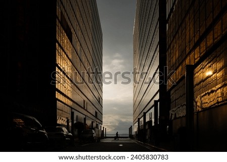 Man walking with a suitcase  in between two office buildings during the sunset Royalty-Free Stock Photo #2405830783