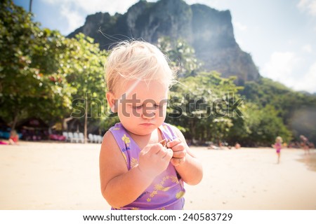 portrait of small blonde baby girl in purple swim suit play on seashore closeup