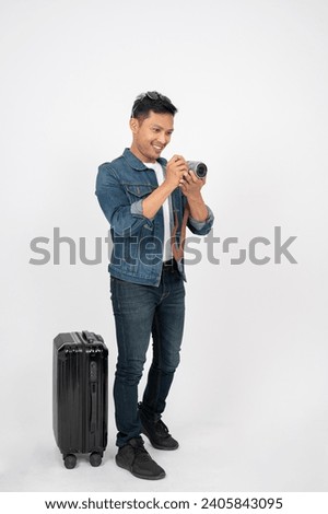 A positive, handsome Asian man tourist is taking pictures with his camera, standing on an isolated white background with his luggage. traveller, tourist, passenger