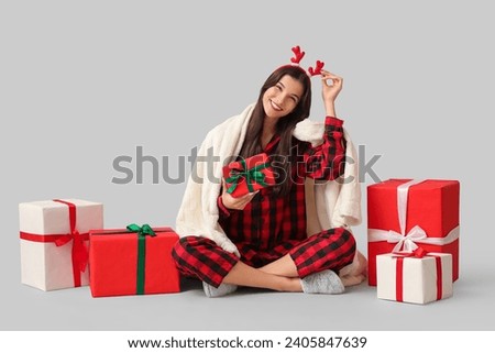Beautiful young woman in checkered pajamas with plaid and Christmas gift boxes on grey background