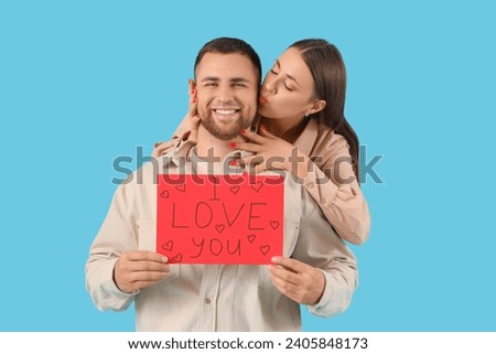 Lovely couple holding greeting card with text I LOVE YOU on blue background. Valentine's Day celebration Royalty-Free Stock Photo #2405848173