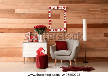 Interior of festive living room with grey armchair, hearts and roses on chest of drawers. Valentine's Day celebration Royalty-Free Stock Photo #2405850293