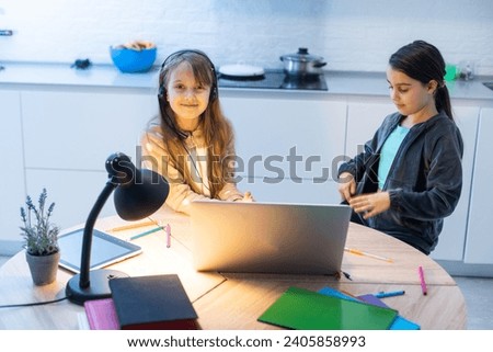 Two child girl students study online with teacher by video call together. Siblings are homeschooling with computer laptop during quarantine due to Covid 19 pandemic.