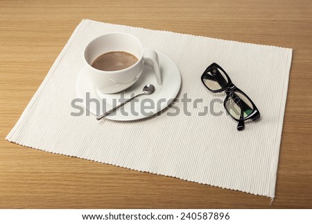 A coffee cup, black glasses on the office desk(table).
