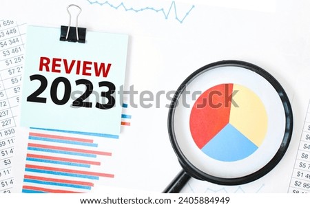 Green card on the white notepad and magnifier on the financial documentation. Text REVIEW 2023 . Business concept