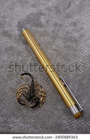 Very stylish, luxurious, velvet, grey notebook, business diary, book with golden stylish pen and with beautiful female brooch black golden scorpion set on white plastic background.