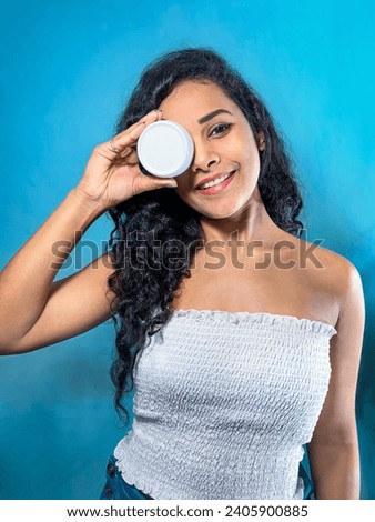 Smiling Indian model with product covering one eye. Photo of Indian woman with blue background. Beauty concept