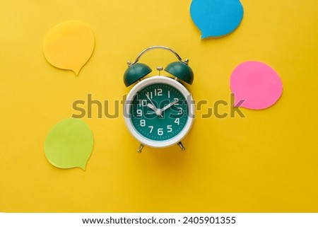 Green classic alarm clock and empty colorful speech bubbles on an yellow background