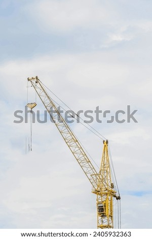 It is yellow tower crane  working in sunny day. There are white clouds in blue sky. It is close up view.  It is a midday time.