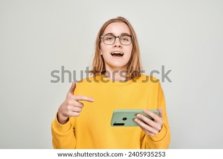 Portrait of young blond woman with mobile phone in hand celebrates victory, winning money in casino. Person with smartphone isolated on white background
