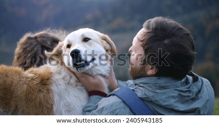 Caucasian couple of hikers sits on the hill, takes photos on phone, pets and plays with local dog. Tourist family during hike or trekking trip in mountains in autumn. Outdoor recreation and travel.
