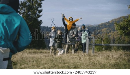Teenage hiker takes group pictures of his multiethnic friends or family on the top of the hill against scenic nature view. Diverse tourists or travelers during hike in mountains. Tourism and travel.