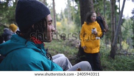 Group of travelers resting in camp after long walking trek in the mountains. Multiethnic young hikers talking, having snack in the forest during tourist trip or hike in autumn. Active leisure concept. Royalty-Free Stock Photo #2405943311