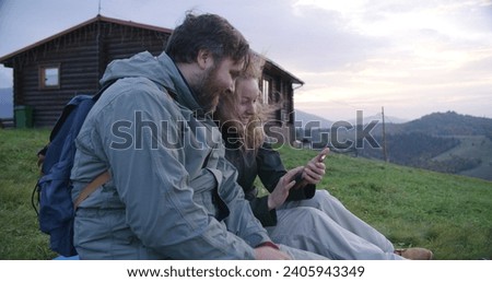 Caucasian couple of hikers sits on the hill with beautiful landscapes, takes pictures and selfie together. Family of travelers during hiking trip or trek in mountains. Tourism and active leisure.