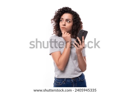 a young slender 30 year old caucasian woman with curly hair in a gray t-shirt uses instant messengers on a smartphone Royalty-Free Stock Photo #2405945335