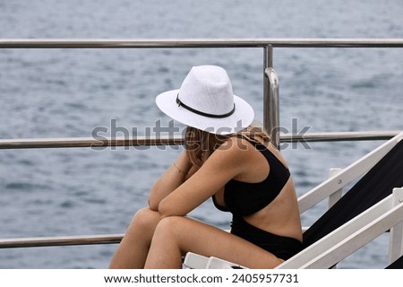 Girl in bikini and sun hat sitting in deck chair on tourist yacht, sea excursion
